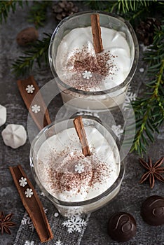 Eggnog in glass cups with a delicate foam, spices and a cinnamon stick