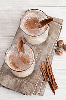 Eggnog in glass cups with a delicate foam, spices and a cinnamon stick
