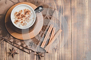 Eggnog. Traditional christmas cocktail in a black mug and cinnamon sticks and anise on a napkin on a wooden background. Copyspace