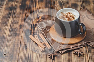 Eggnog. Traditional christmas cocktail in a black mug and cinnamon sticks and anise on a napkin on a wooden background. Copyspace