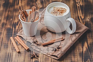 Eggnog. Traditional christmas cocktail in a white mug with cinnamon sticks  and anise on a napkin. Wooden background