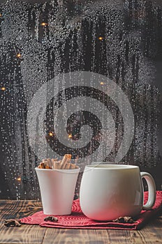 Eggnog. Traditional christmas cocktail in a white mug with cinnamon sticks and anise on red solfette and wooden table. Background