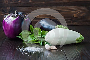 Eggplant (aubergine) with basil and garlic on dark wooden table. Fresh raw farm vegetables - harvest from the garden in