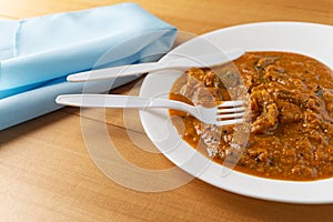 Eggplant curry meal on a white plate with plastic silverware