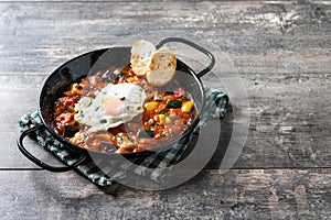Eggplant and egg, onions, peppers, served in frying pan on wooden table, Vegetable pisto manchego with tomatoes, zucchini