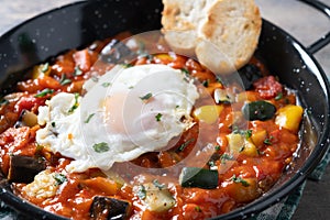 Eggplant and egg, onions, peppers, served in frying pan on wooden table, Vegetable pisto manchego with tomatoes, zucchini