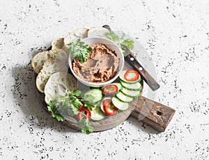 Eggplant, smoked paprika, walnuts dip, vegetables and bread on wooden cutting board on a light background.