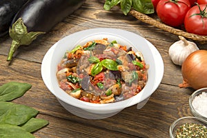 Eggplant stew with tomatoes and spinach in a salad bowl on a rustic table with ingredients.