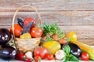 Eggplant, tomatoes in a wicker basket, carrots and other vegetables on a wooden background