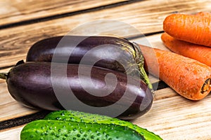 Eggplants, carrots and cucumbers on a wooden background