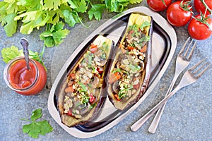 Eggplants stuffed with mushrooms, onions, carrots, tomatoes and nuts on a metal plate on a grey background. Vegetarian food. healt