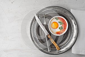 Eggs baked with tomatoes and parsley in the ramekins with cutlery top view photo