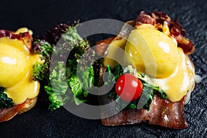 Eggs Benedict with bacon on volcanic rock background