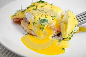 Eggs Benedict for breakfast on a white plate, liquid yolk