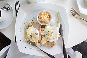 Eggs benedict breakfast on white plate and table with silverware