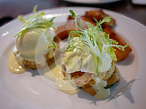 Eggs Benedicts hollandaise sauce with nice decorated and potato wedges or home fries in white plate served in restaurant or cafe