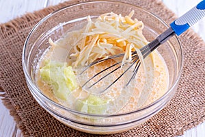 Eggs in a bowl with whisk and cheese on a wooden table