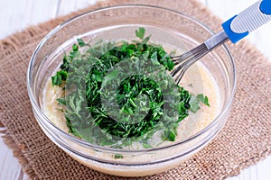 Eggs in a bowl with whisk and greens on a wooden table