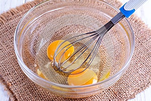 Eggs in a bowl with whisk on a wooden table