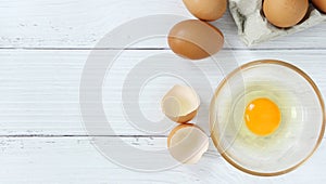 Eggs in a clear cup around with a shell and an egg in a paper plate on a white wooden table in top view.
