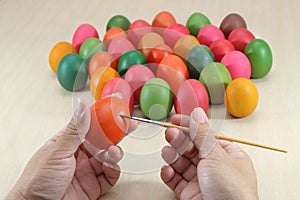 Eggs are painted by hands of person against paintbrush on marble top preparing for easter day.