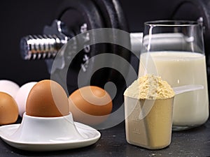 eggs, scoop of whey protein powder, glass of milk and dumbbell on black background, concept of sports nutrition