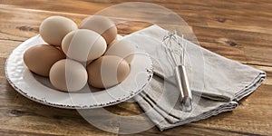 Eggs, whisk, napkin, wooden background.