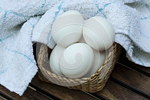 Eggs in a wooden basket with white napkin on wooden table.