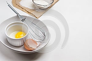 Eggshell, egg and whisk in bowl. Egg yolk in bowl. Flour and sieve on paper