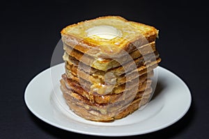 Eggy bread on a black background. Butter melts on a stack of eggy breads.