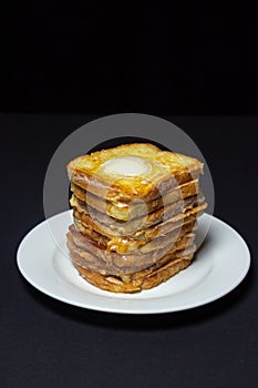 Eggy bread on a black background. Butter melts on a stack of eggy breads.