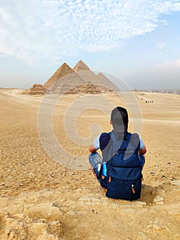 Egypt. Cairo Giza. young blonde tourist girl with a backpack is sitting on the sand looking at General view of pyramids from the