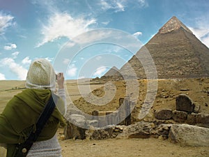 Egypt. Cairo. Giza.The young woman makes a photo of pyramids. She is standing back to the camera. The blue sky with a clouds and s