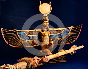 Egyptian goddess Isis kneeling with traditional magic wand made with quartz, amethyst crystals, wood and feathers