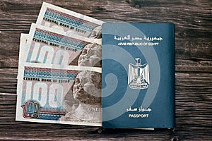 Egyptian passport with 100 EGP LE one hundred Egyptian pounds money banknotes isolated on wooden background