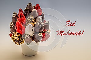 Eid Mubarak greeting card with red lettering; A bundle of edible flowers, arrangement of strawberries covered with chocolate