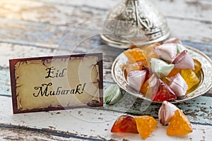 Eid mubarak text on greeting card on vintage table with candies