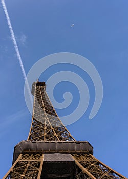 Eiffel Tower from below against the clear blue sky with contrail and airplane