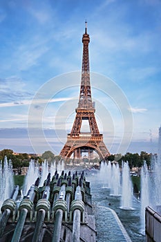 Eiffel Tower, iconic Paris landmark with setting sun and vibrant blue summer skies with fountain and sprinkling water