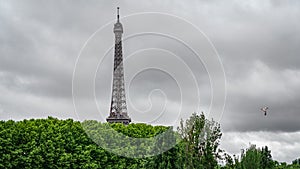 The Eiffel Tower over trees with stormy clouds