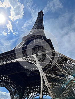 The Eiffel Tower in Paris from the base, under a blue cloudy sky