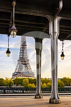 The Eiffel tower in Paris, France, with the pillars and street lights of the Bir-Hakeim bridge in the foreground by a sunny