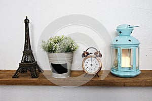 Eiffel tower statue, artificial plant, vintage alarm clock and blue lantern with LED candle light on wooden shelves