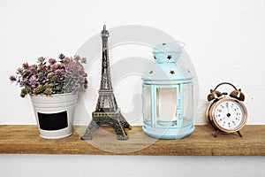 Eiffel tower statue, artificial plant, vintage alarm clock and blue lantern with LED candle light on wooden shelves