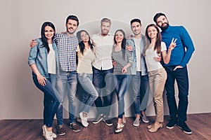 Eight happy friends are posing near the wall, smiling and gesturing, wearing casual outfits, so trendy and stylish, attractive