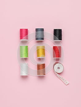 Eight multicolored coils with threads and a measuring tape on a pink background. Flat lay