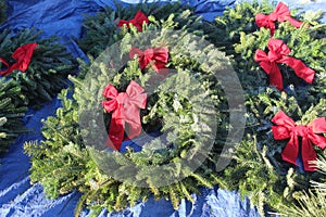 Eight natural Christmas wreaths decorated with red bows lying on a tarp.