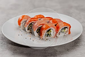 Eight servings of sushi with salmon and cucumber on a white plate.
