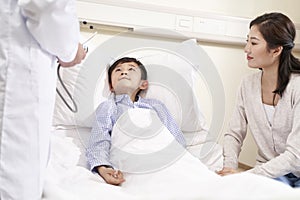 Eight year old asian kid lying in bed in hospital ward accompanied by mother