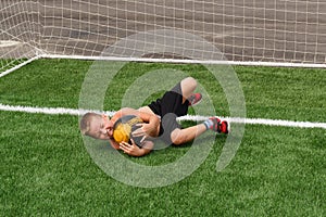 An eight-year-old boy in black shorts catches a soccer ball in the goal